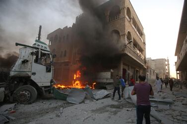 People walk amidst rubble as part of a building burns following a reported airstrike by Syrian regime forces in Maaret Al Numan, Idlib.  AFP