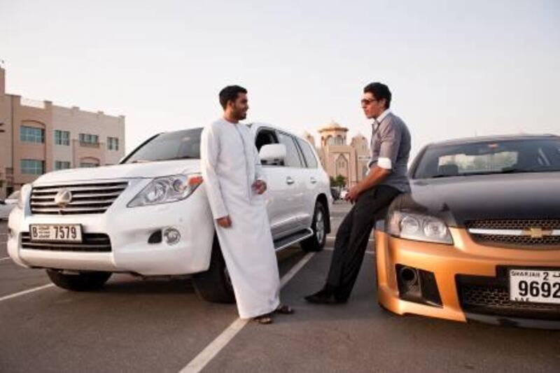 Aref al Mazrooei, 21 (in kandoura) and Ahmed al Saadi, 20, both students of American University in the Emirates talk in the parking lot with their cars. Photo by Siddharth Siva for The National 