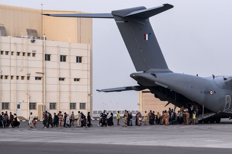 People walk on the tarmac as they disembark from a Airbus A400M military transport aircraft at the French military air base 104 of Al Dhafra, near Abu Dhabi, on August 23, 2021, after being evacuated from Kabul as part of the operation "Apagan".  (Photo by BERTRAND GUAY  /  AFP)
