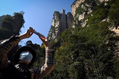 This picture taken on November 13, 2020 shows a tourist with a face mask using her mobil phone to take a picture at the entrance of the Bailong elevators in Zhangjiajie, China's Hunan province.   Towering more than 300 metres (1,000 feet) up the cliff face that inspired the landscape for the blockbuster movie "Avatar", the world's highest outdoor lift whisks brave tourists to breathtaking views. - TO GO WITH: China technology film tourism transport, by Ludovic EHRET
 / AFP / WANG ZHAO / TO GO WITH: China technology film tourism transport, by Ludovic EHRET
