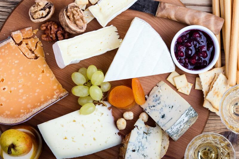 Cheese platter with fruits and wine on wooden table viewed from above, delicious holiday appetizer