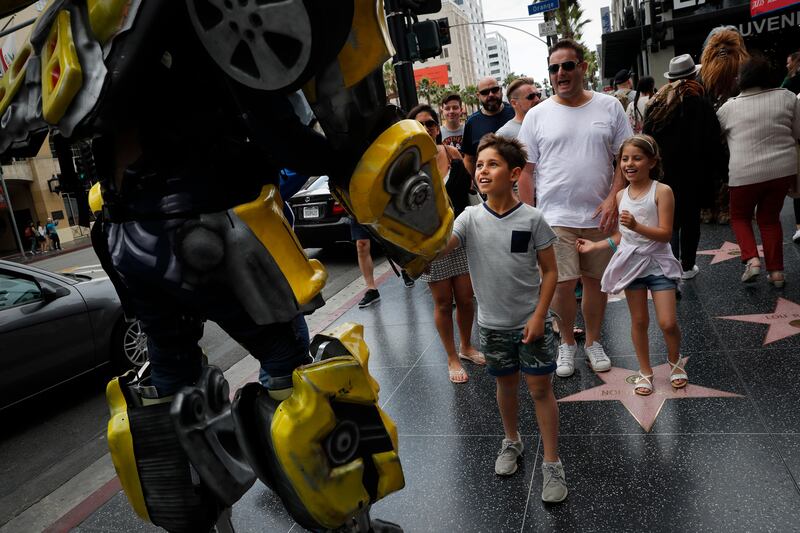 Ramiro Rodriguez in a Bumblebee costume, a character from the Transformers movie series, shakes hands with young tourists on Hollywood Boulevard, in Los Angeles. The 39-year-old former restaurant worker from Guadalajara, Mexico, changed his career after watching a film on Hollywood characters. Rodriguez and his brother invested all their savings in the costume. Even on bad days, Rodriguez said they still make enough to buy dinner. Jae C Hong / AP Photo