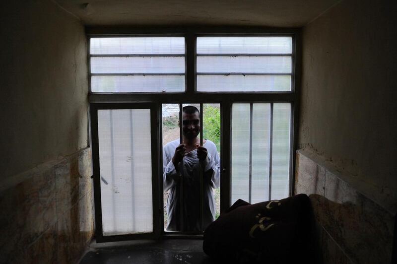 A patient holds protective bars while looking through the window to the back of his room.