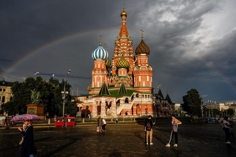 Russians walk in front of St Basil Cathedral lit by the sun with a rainbow in the background on Red Square, Moscow. AFP