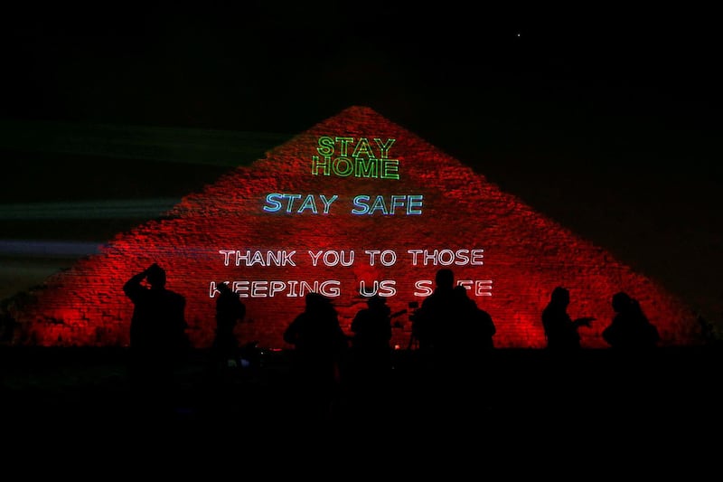 People are seen in front of the pyramid of Khufu, the largest of the Giza pyramid complex, illuminated with text encouraging people to stay home, as Egypt ramps up its efforts to slow down the spread of the coronavirus outbreak, in Giza, on the outskirts of Cairo, Egypt. Reuters