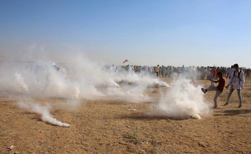 A protesters try to kicks back a teargas canister while others run to cover from teargas fired by Israeli troops near the fence of the Gaza Strip border with Israel, during a protest east of Khan Younis, southern Gaza Strip, Friday, Aug. 17, 2018.  Two Palestinians were killed by Israeli fire and another 60 injured at a protest along the Gaza border amid ongoing Egyptian efforts to broker a cease-fire, Gaza's Health Ministry said Friday. (AP Photo/Adel Hana)