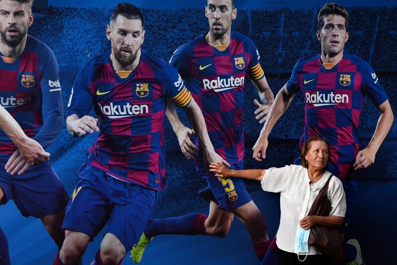 A woman touches the hand of Barcelona's Argentinian forward Lionel Messi, depicted on a poster with teammates Spanish defender Gerard Pique (L), Spanish midfielder Sergio Busquets (2R) and Barcelona's Spanish defender Sergi Robert, outside the Camp Nou stadium in Barcelona on September 4, 2020. Lionel Messi confirmed today he will stay at Barcelona, insisting he could never go to court against "the club of his life". Messi released a statement at 6pm CET, saying "I would never go to court against Barca because it is the club that I love, that gave me everything since I arrived, it is the club of my life, I have made my life here." / AFP / Pau BARRENA
