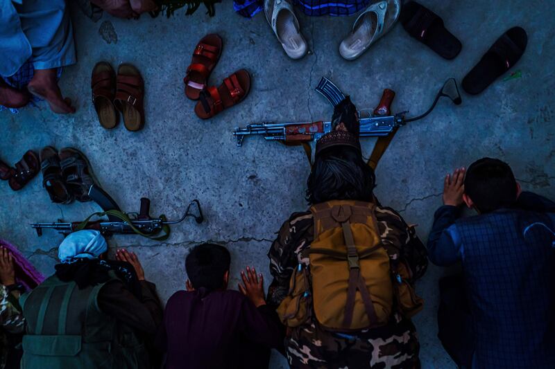 Taliban fighters pray next to young Afghans outside a local mosque for evening prayers in Kabul, Afghanistan, on August  26, 2021. By Marcus Yam. Los Angeles Times/EPA
