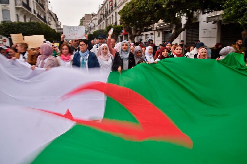 TOPSHOT - Algerians carry a giant national flag as they take part in a demonstration in the capital Algiers against President Abdelaziz Bouteflika on March 19, 2019.  Bouteflika today confirmed he will stay in power beyond his term expiring next month, despite tens of thousands of people demonstrating against his rule. / AFP / RYAD KRAMDI                        
