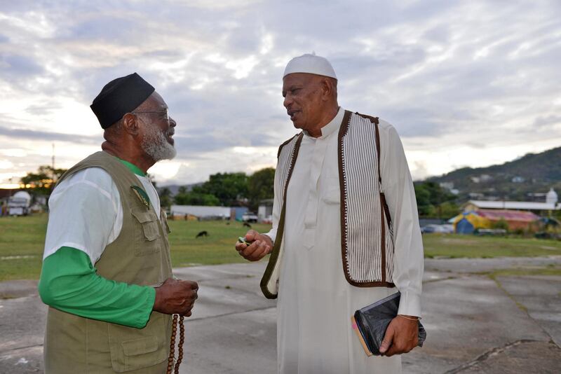 In this photo taken May 3, 2013, Yasin Abu Bakr, right, who led a small army that stormed Trinidad & Tobago���s parliament in 1990, speaks with a fellow member of his group, Jamaat al Muslimeen, at their compound in Port-of-Spain, Trinidad.  Bakr, never convicted of any charges, presides over a mosque and school complex in the country's capital, and shares time among his four wives, the maximum Islam allows. Bakr said he hasn���t decided if he���ll testify before the five-member  commission, which is expected to finish collecting testimony by year���s end. (AP Photo/David McFadden)