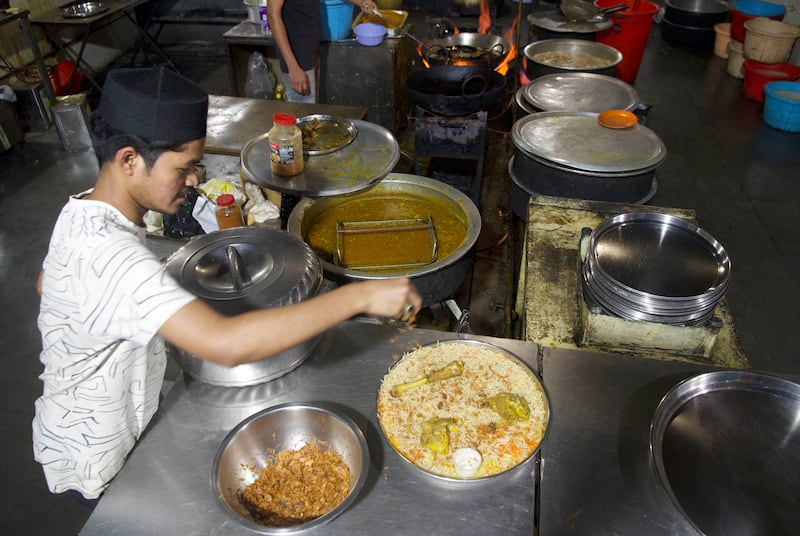 A restaurant server assembles a large plate of mandi, a traditional Yemeni meat and rice dish