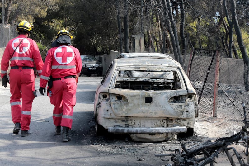 Members of the Red Cross search the area past burned cars after a fire in Argyra Akti, Mati. EPA