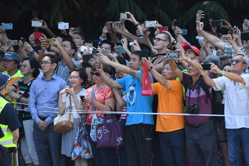 Bystanders take pictures of the motorcade transporting US president Donald Trump as it drives towards the Istana. Adek Berry / AFP