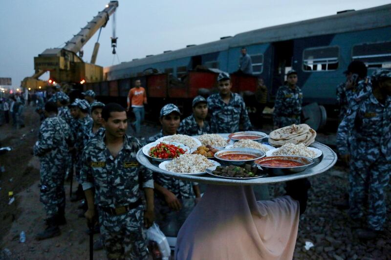 A woman takes food for security forces to break their fast during Ramadan at the site of a passenger train accident near Banha, Qalyubia province, Egypt. AP