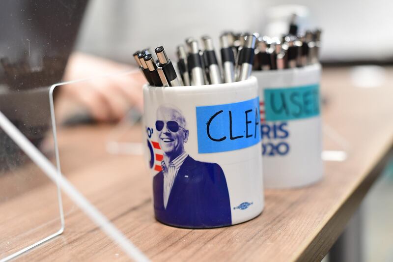 A lab technician works behind pens placed in themed President-elect Joe Biden mugs that state "CLEAN" and "USED" at a coronavirus (COVID-19) testing location for media in Wilmington, Delaware.  AFP