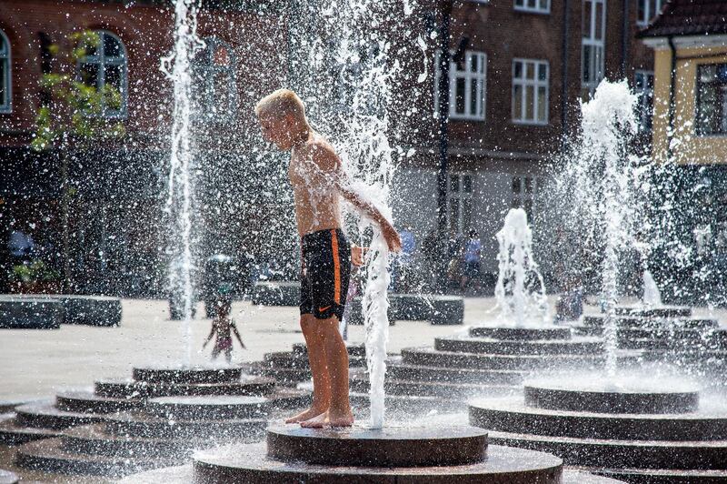 A boy enjoys a bath in the fountain at Toldbod Plads in Aalborg, Denmark, while the thermometer shows 30 degrees Celsius. EPA