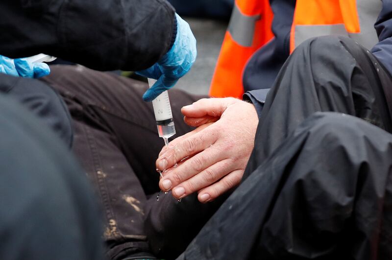 A police officer applies a solution on the glued hands of an Insulate Britain activist. Reuters