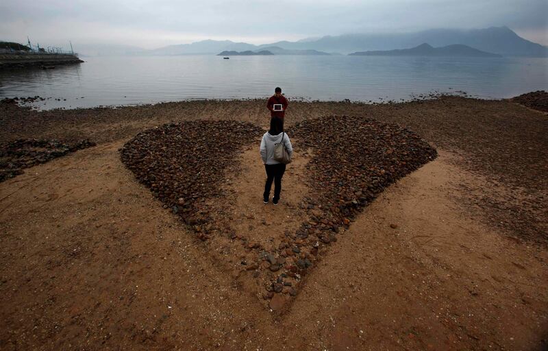 A man shows a tablet computer, with its screen displaying "I love you" in Chinese, to his girlfriend on a heart-shaped sculpture made of six by seven metres of sand and stone, during low tide at a beach in Hong Kong on Valentine's Day February 14, 2012.  REUTERS/Bobby Yip   (CHINA - Tags: SOCIETY TPX IMAGES OF THE DAY) *** Local Caption ***  HKG02_CHINA_0214_11.JPG
