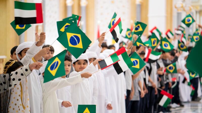 Children welcome President Jair Bolsonaro to Al Shati Palace with Emirati and Brazilian flags.