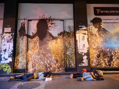 A family sleeps outside a building with a bank advertisement plastered on the facade. Photo: Hussein Baydoun