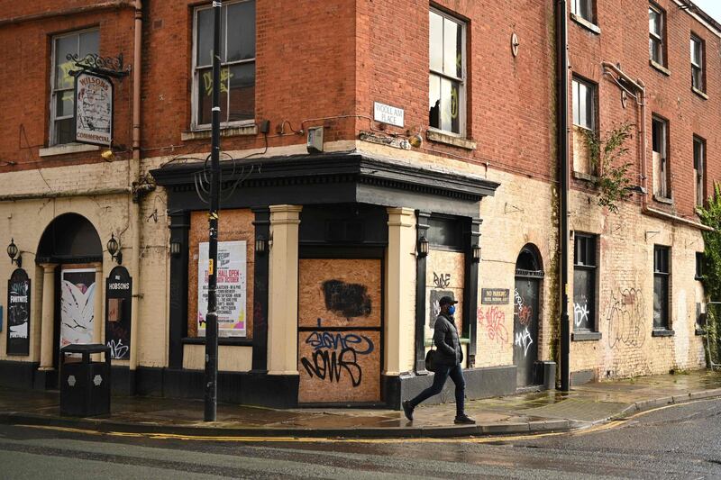 A pedestrian wearing a face mask as a precaution against the transmission of the novel coronavirus walk pasts a derelict pub in Manchester, north west England on October 13, 2020, as the number of cases of the novel coronavirus COVID-19 continue to rise. The British government faced renewed pressure on October 13, after indications it had ignored scientific advice three weeks ago for tougher restrictions to cut rising coronavirus infections. / AFP / Oli SCARFF
