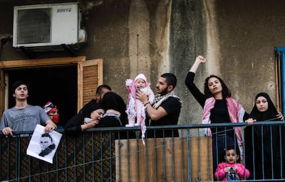 Family members of Lebanese protester Fawwaz al-Samman -- who died after he was shot during riots in late April -- hold up his infant girl and react as they stand in their balcony as protesters coming from acrosss the country gather for a demonstration outside his family home in the northern port city of Tripoli on May 3, 2020.  / AFP / Ibrahim CHALHOUB
