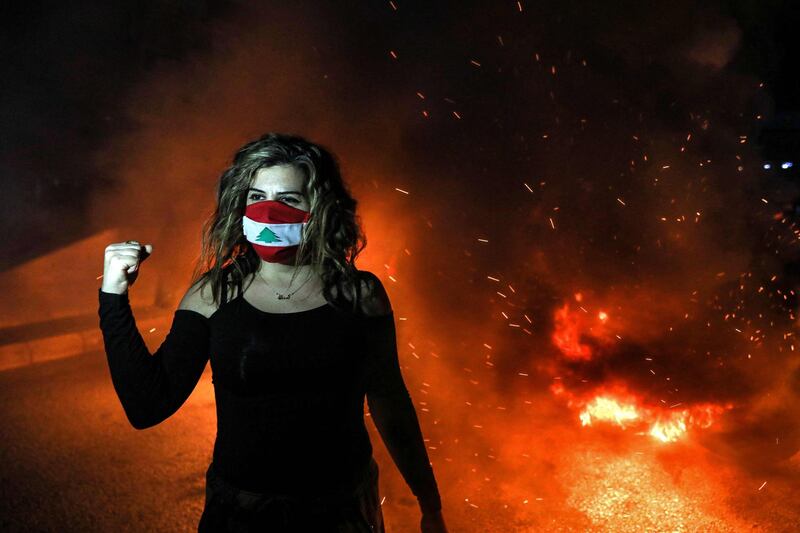 A demonstrator clad in mask coloured with the Lebanese flag reacts as she stands next to flaming tires cutting off a road in the centre of Lebanon's capital Beirut. AFP
