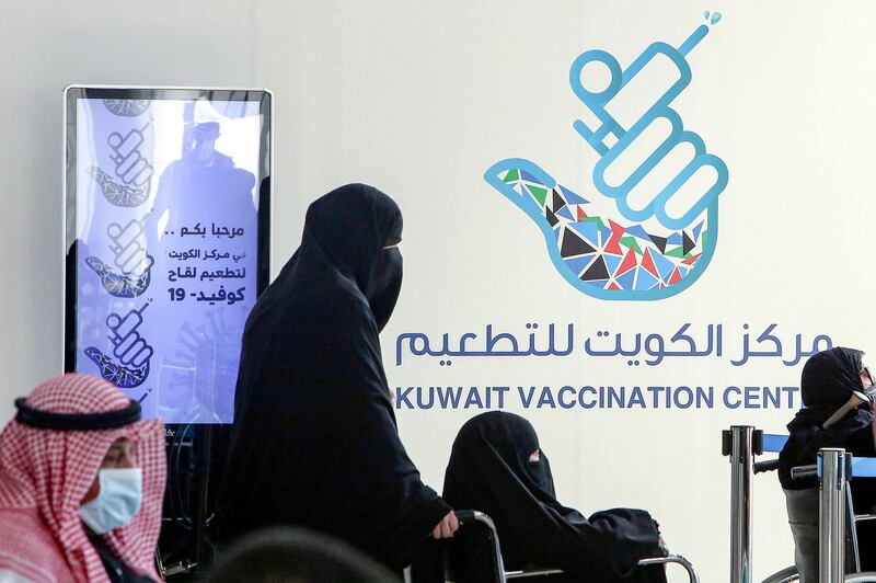 A woman pushes another in a wheelchair as they queue to register before receiving a dose of COVID-19 coronavirus vaccine at the make-shift vaccination centre erected at the Kuwait International Fairground, in the Mishref suburb south of Kuwait City on February 1, 2021.  Kuwait received on February 1 a shipment of 200,000 doses of Oxford-AstraZeneca vaccine. / AFP / YASSER AL-ZAYYAT

