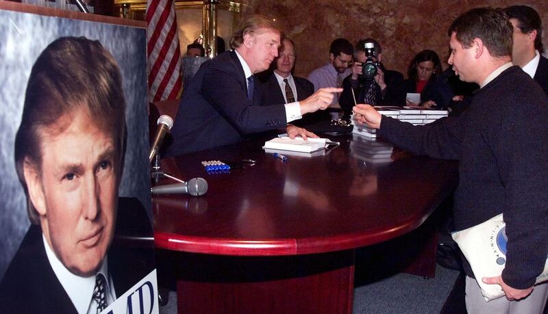 Donald Trump reaches for a pen as he signs a copy of his new book "Trump, The America We Deserve" during a book signing at Trump Towers 05 January, 2000 in New York, NY.            AFP PHOTO/MATT CAMPBELL (Photo by MATT CAMPBELL / AFP)