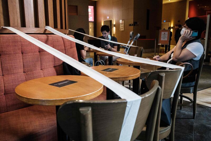 Customers wearing face masks as a precautionary measure against the COVID-19 coronavirus sit in a cafe, which has masking tape on every other table to enforce social distancing, in Hong Kong.  AFP