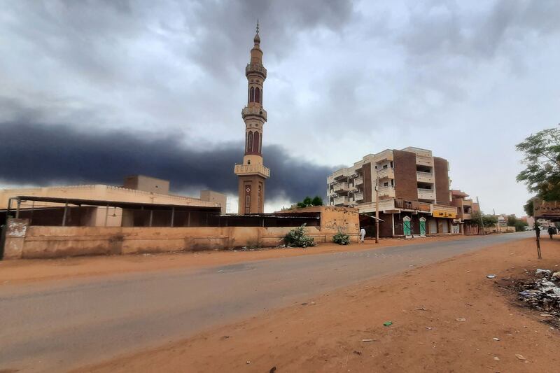 Smoke rises above buildings behind a nearly deserted street in Khartoum on Saturday.  AFP