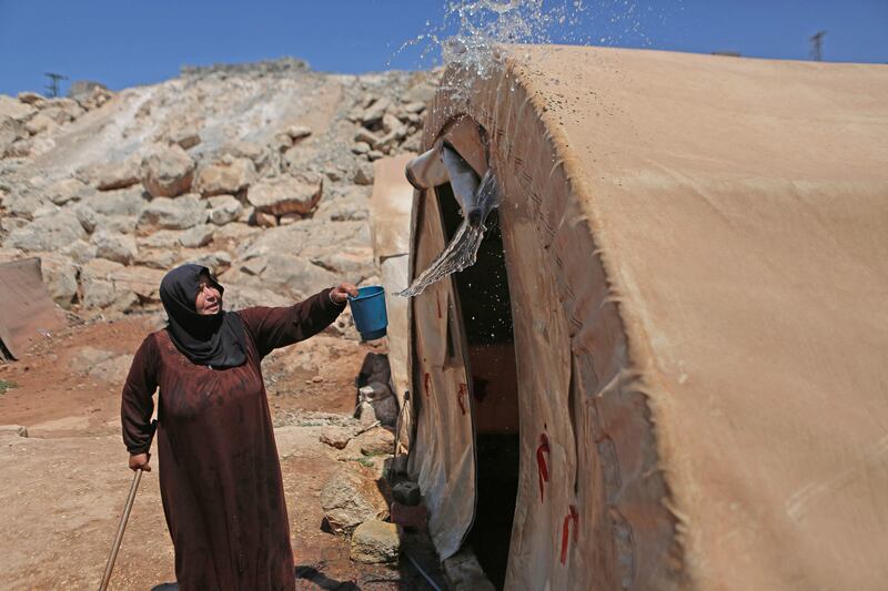 A woman cools down her tent with water amid soaring temperatures in a camp near Syria's Bab Al Hawa border area with Turkey.  