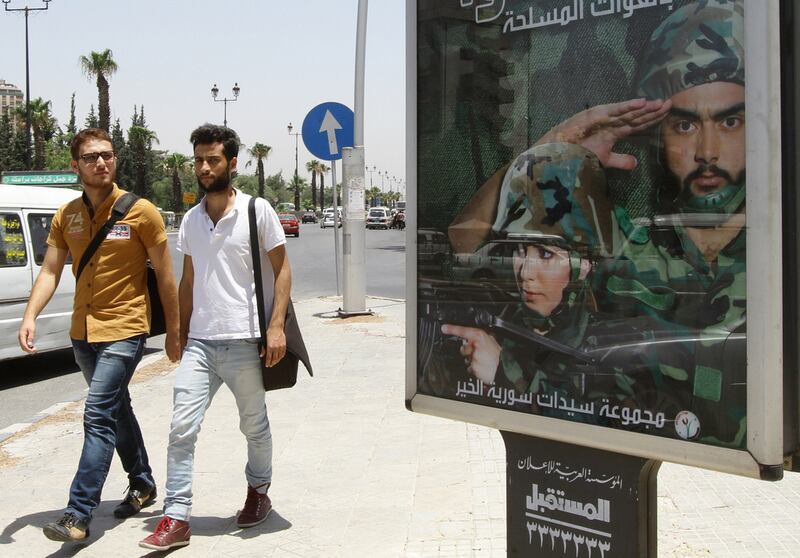 Two men walk past a billboard in the Syrian capital Damascus, which calls on young men and women to enlist in the country's army. Louai Beshara/AFP Photo 


