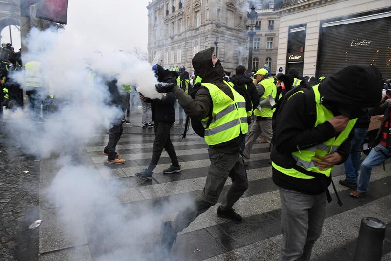A demonstrator throws a tear gas canister during the demonstration of the yellow vests at the Arc de Triomphe. Getty Images