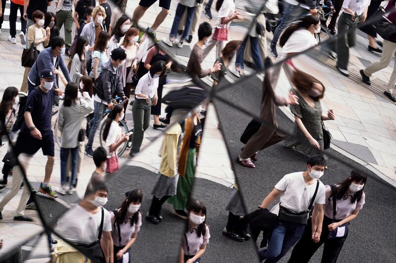 People wearing protective masks to help curb the spread of the coronavirus are reflected on the mirror wall of a shopping mall in Tokyo.  AP