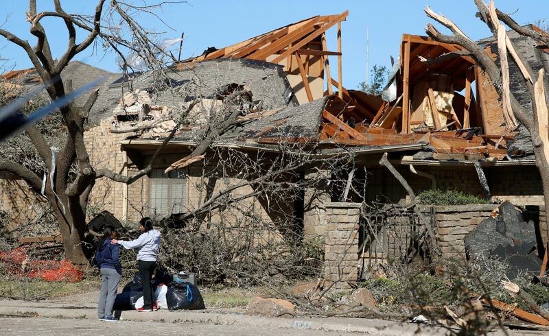 Women stand outside a house damaged by a tornado in the Preston Hollow section of Dallas. AP Photo