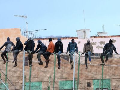 (FILES) In this file photo taken on February 19, 2015 migrants sit atop a border fence separating Morocco from the north African Spanish enclave of Melilla in the first attempt to jump since the camp on Mount Gurugu burned down.  A migrant died on October 21, 2018 after around 200 people scaled a fence to enter Spain's Melilla enclave from northern Morocco, local Spanish authorities said. / AFP / ANGELA RIOS
