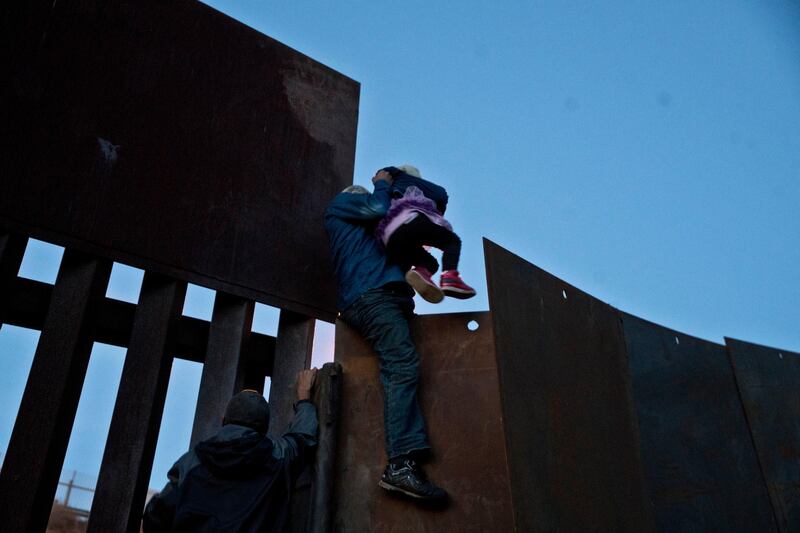 A Honduran migrant helps a young girl cross to the American side of the border wall, in Tijuana, Mexico. AP Photo