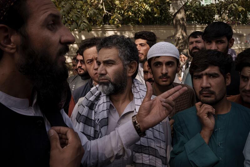 A member of the Taliban, left, talks to Afghans gathering outside a government passport office. Photo: AP