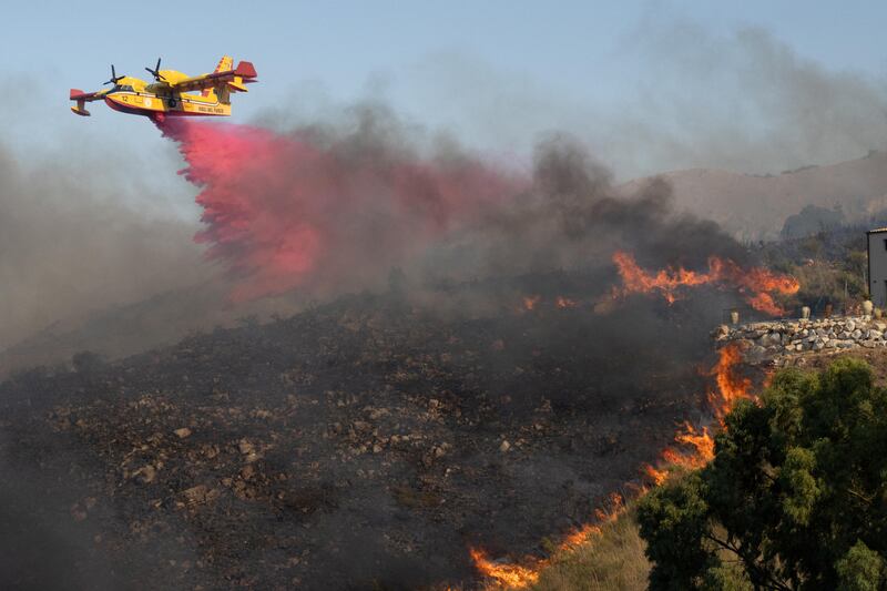 A plane drops flame retardant on burning vegetation in Sicily, Italy. Reuters