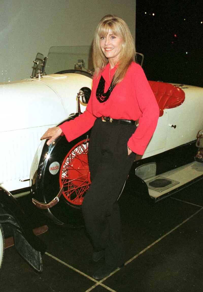 Jane Fonda, in a red blouse and black trousers, stands next to a Rolls-Royce at a dinner held in her honour at the automobile museum, Los Angeles, California, on November 10, 1996