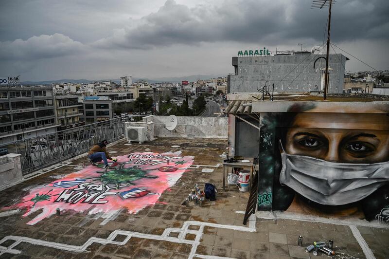 A youth artist S.F. paints a mural about the Covid-19 crisis on the roof of his building in Athens. AFP