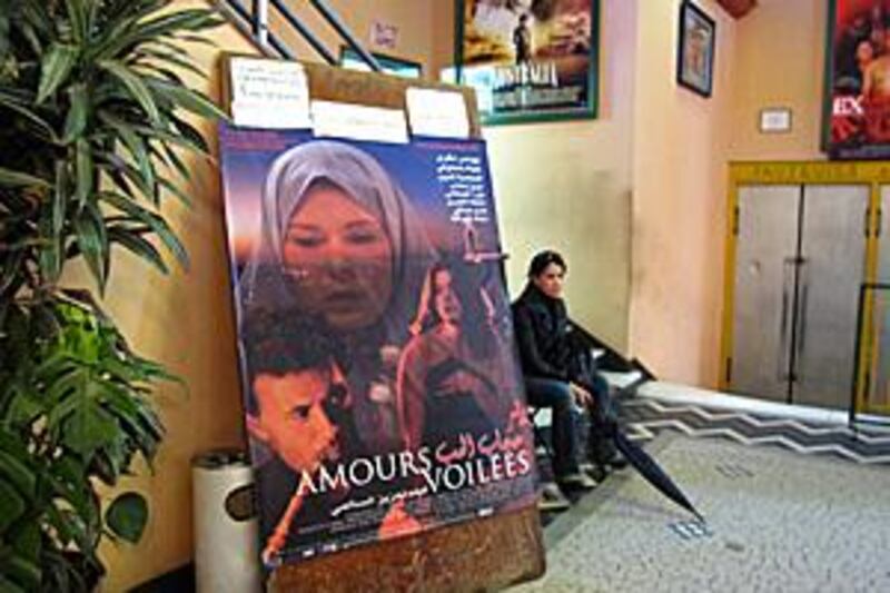 A woman sits beside a giant poster for Amours Voilées at a cinema in the Moroccan capital, Rabat.