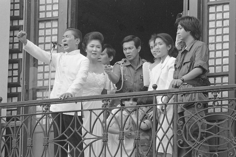 President of the Philippines Ferdinand Marcos, with his wife Imelda at his side, gestures from the balcony of Malacanang Palace, Feb. 25, 1986, after taking the oath of office. Hours later, Marcos resigned and fled to the U.S. Air Force's Clark Air Base, 50 miles northwest of Manila, as he prepared to accept an American offer to fly him out of the Philippines. (AP Photo/Alberto Marquez)
