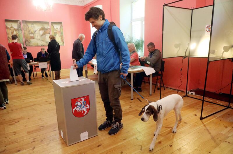 A voter with a dog casts his ballot during the first round of Lithuania's presidential election. AFP
