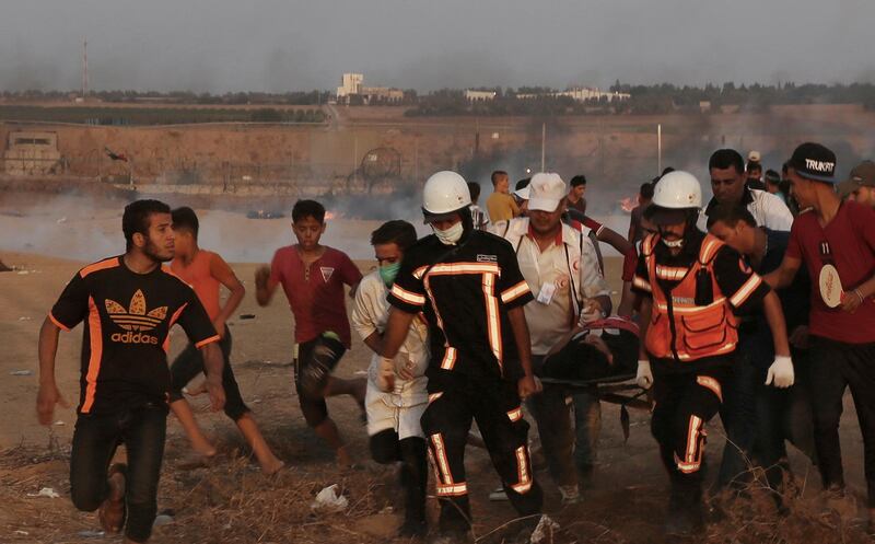 Medics evacuate their wounded colleague, who was shot in his chest, from near the fence of Gaza Strip border with Israel during a protest east of Khan Younis, southern Gaza Strip, Friday, Oct. 5, 2018. Israeli forces shot dead three Palestinians, including a 13-year-old boy, as thousands of people protested Friday along the fence dividing the Gaza Strip and Israel, Gaza's Health Ministry said. (AP Photo/Adel Hana)