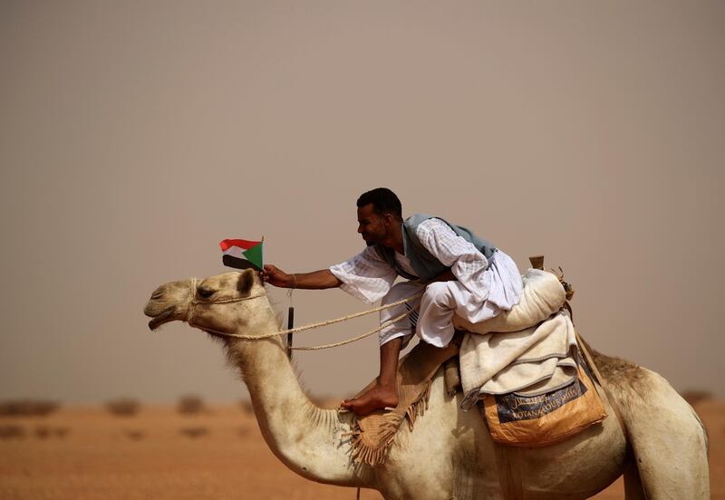 A supporter of Lieutenant General Mohamed Hamdan Dagalo, deputy head of the military council and head of paramilitary Rapid Support Forces (RSF), attaches a Sudanese national flag to the head of his camel during a meeting in Aprag village. Reuters