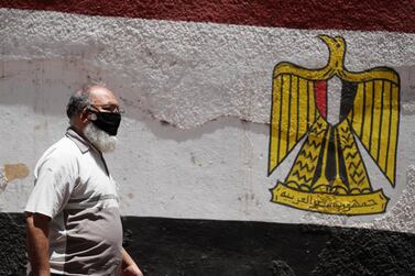 A man wearing a protective face mask walks next to a wall painted with the colours of Egypt's flag. The country's latest funding comes on top of the $2.8bn the International Monetary Fund board approved last month to help it cope with the fallout from the Covid-19 pandemic. Reuters