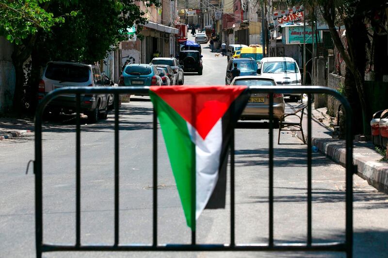 A Palestinian flag is draped over a metal barrier at a checkpoint at the entrance of Amari refugee camp near the West Bank city of Ramallah on July 24, 2020. A second wave of coronavirus infections sweeping the Israeli-occupied West Bank is fuelling fears of a surge in overcrowded Palestinian refugee camps where social distancing is widely seen as impossible. The Palestinian health ministry's Tuesday update logged more than 10,860 confirmed cases of infection since the start of the pandemic, including more than 75 deaths. / AFP / ABBAS MOMANI
