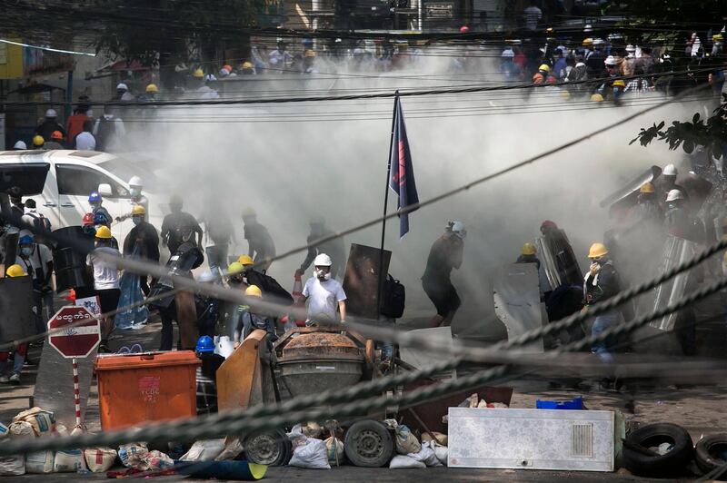 Anti-coup protesters gathered behind a barricade are enveloped by tear gas during a demonstration in Yangon. AFP